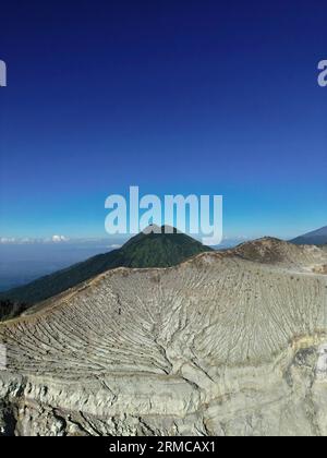 Splendido paesaggio montano del vulcano Ijen con una montagna di roccia cratere, vegetazione lussureggiante, una valle e un cielo azzurro. Foto Stock