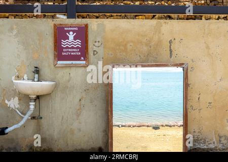 Attenzione cartello acqua estremamente salata sulla spiaggia di Dead Sea Jordan, lavello per lavarsi dopo aver nuotato in acqua salata, muro con la porta vista sul mare Foto Stock