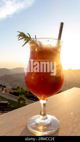 Bicchiere di frullato di succo di fragole con cannuccia contro il sole Foto Stock