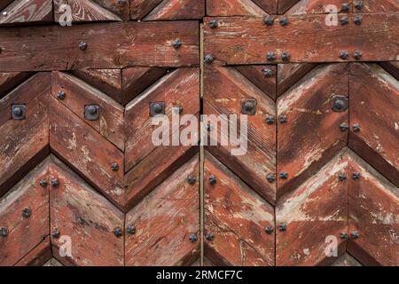 porta in legno verniciata marrone composta da tavole zigzag. si tratta di una fodera chiodata con rivetti o chiodi metallici Foto Stock