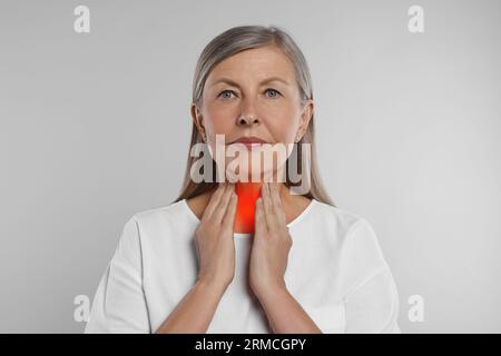 Sistema endocrino. Donna anziana che fa autoesame della tiroide su sfondo grigio chiaro Foto Stock