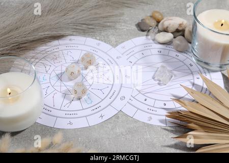 Ruota zodiacale, carta natale, candele in fiamme, dadi astrologici e pietre su tavolo grigio Foto Stock