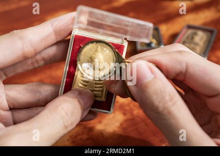 Usando una lente di ingrandimento per vedere i dettagli su un vecchio amuleto di Buddha tailandese Foto Stock