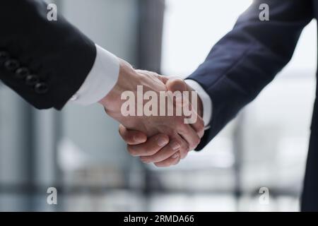 Uomini d'affari che scuotono le mani in piedi davanti alle finestre dell'ufficio Foto Stock