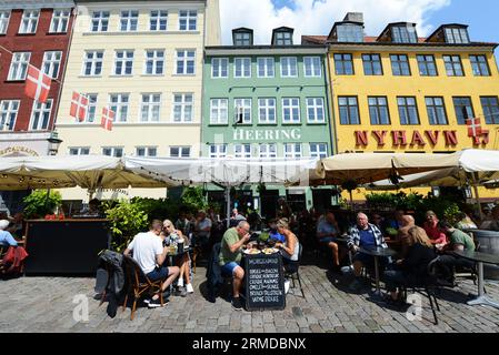 Bar e ristoranti che costeggiano il lato settentrionale e soleggiato di Nyhavn, Copenhagen, Danimarca. Foto Stock