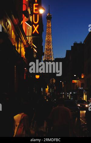 La Torre Eiffel al tramonto, il cielo blu, i lampioni, un cartello rosso al neon, persone e automobili e la silhouette di Rue Saint-Dominique, una calda notte d'estate a Parigi Foto Stock