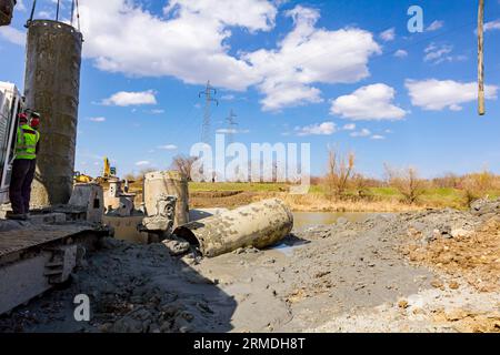 Perforatrice a torre industriale, con attrezzature di grandi dimensioni per perforare nel terreno, per la fondazione di ponti sulla costa del fiume. Foto Stock
