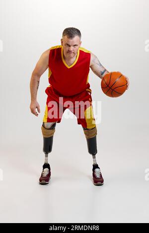 Uomo attraente e sicuro con disabilità protesica alle gambe con pallina da basket arancione in movimento. Sport inclusivo per disabili. Foto Stock
