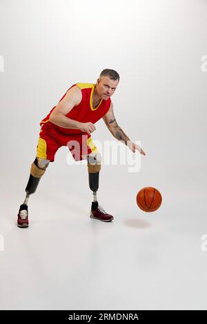 Uomo attraente, sicuro e sportivo con gambe protesiche, disabilità con pallina da basket arancione in movimento. Sport inclusivo per disabili Foto Stock