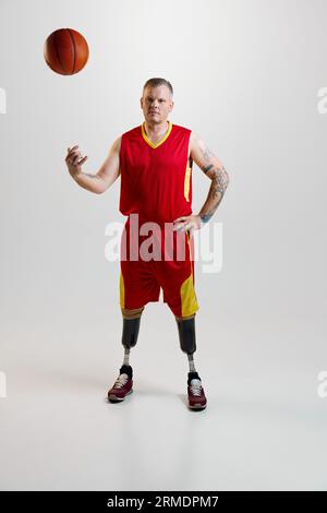 Uomo sicuro e sportivo con gambe protesiche, disabilità in uniforme lancia la palla da basket. Sport inclusivo per disabili. Foto Stock