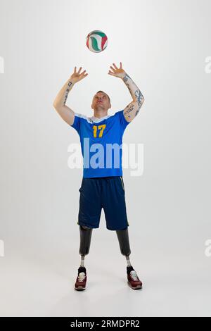 Giovane attraente con disabilità protesica alle gambe in piedi tira su pallavolo. Sport inclusivo per disabili. Foto Stock