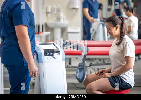 Medico che utilizza la macchina per trattare le articolazioni del ginocchio di un paziente. Foto Stock