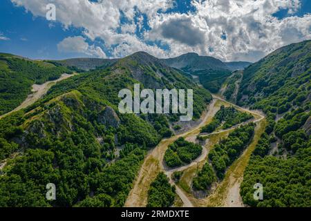 Vista aerea di una strada tortuosa che attraversa un terreno erboso e montuoso Foto Stock