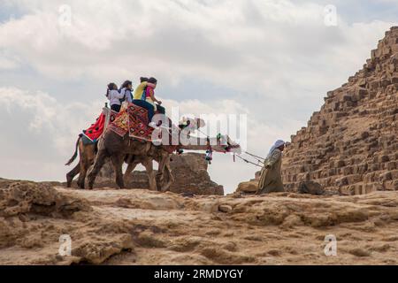 Giovani adolescenti che cavalcano a dorso di cammelli alle piramidi di Giza Foto Stock