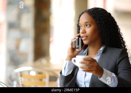 Donna d'affari nera che parla al telefono seduto sulla terrazza di un bar Foto Stock