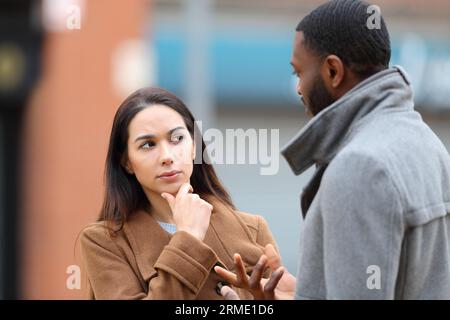 Donna dubbiosa che ascolta un uomo che parla per strada in inverno Foto Stock