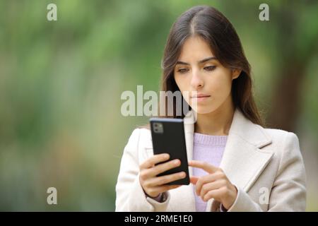 Donna seria che usa il telefono in inverno fuori a camminare in un parco Foto Stock