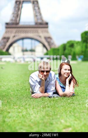 Primo piano di una felice coppia positiva stesa sull'erba vicino alla Torre Eiffel Foto Stock