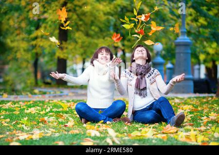 Madre e figlia insieme nel parco in una luminosa giornata autunnale, divertendosi e lanciando foglie autunnali in aria Foto Stock