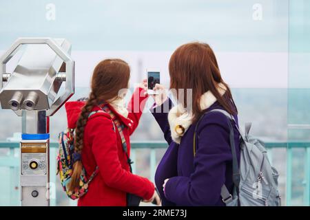 Due ragazze allegri a Parigi, che si fotografano l'una sull'altra sulla piattaforma di osservazione della torre di Montparnasse con il cellulare Foto Stock