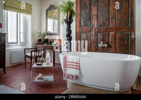 Le porte in legno recuperate nascondono la doccia con torchere ornate e lavabo vintage nel bagno Cotignac, Var, Francia. Foto Stock