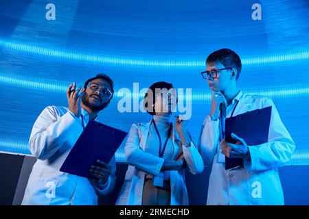 soluzioni futuristiche, scienziati multietnici con appunti che parlano in un centro di scoperta illuminato al neon Foto Stock