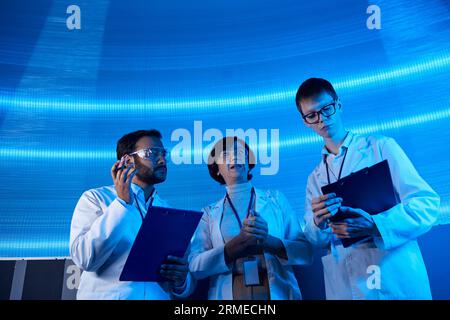 scienziati multietnici con clipboard che lavorano su tecnologie futuristiche nel centro scientifico Foto Stock