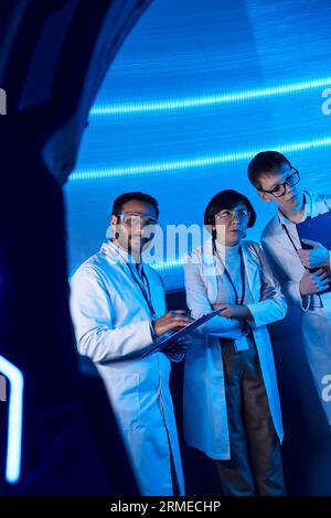 scoperte scientifiche, scienziati multietnici vicino ad attrezzature sperimentali, centro scientifico futuristico Foto Stock