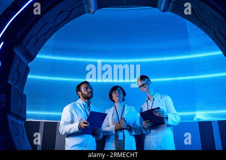 apparecchiature innovative futuristiche, scienziati multietnici con clipboard vicino a dispositivi sperimentali Foto Stock