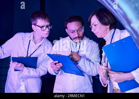 Futuristic Analysis: Scientists of Varied Ages Compare Data in Neon-Lit Science Center Stock Photo