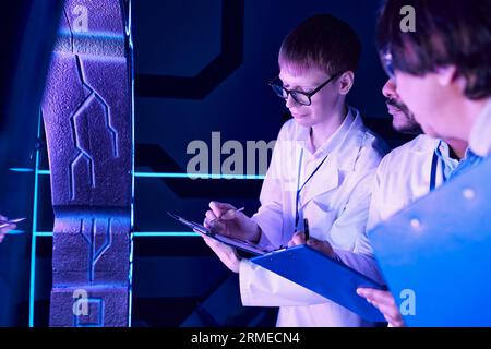 Collaborazione futuristica: Scienziati di età diversa lavorano vicino al dispositivo nel Neon-Lit Science Center Foto Stock