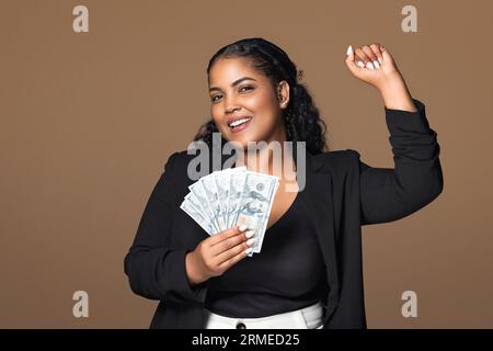 Eccitata donna d'affari brasiliana più grande in possesso di denaro contante e gestante sì, celebrando il successo e l'aumento dello stipendio Foto Stock