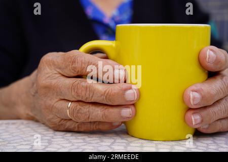 donna matura irriconoscibile che beve una tazza gialla. Stile di vita anziano con rughe Foto Stock