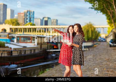 Bellissime sorelle gemelle con abiti a pois rossi e neri vicino al fiume Senna a Parigi, Francia, utilizzando la mappa Foto Stock