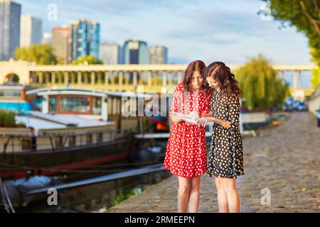 Bellissime sorelle gemelle con abiti a pois rossi e neri vicino al fiume Senna a Parigi, Francia, utilizzando la mappa Foto Stock