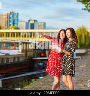 Bellissime sorelle gemelle con abiti a pois rossi e neri utilizzando una mappa vicino al fiume Senna a Parigi, Francia Foto Stock