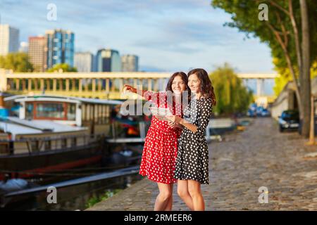 Bellissime sorelle gemelle con abiti a pois rossi e neri utilizzando una mappa vicino al fiume Senna a Parigi, Francia Foto Stock