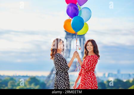 Bellissime sorelle gemelle in abiti a pois rossi e neri con enormi palloncini colorati di fronte alla Torre Eiffel a Parigi, in Francia Foto Stock