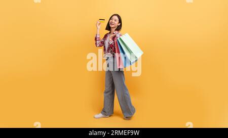 Concetto di shopping illimitato. Signora asiatica che tiene borse colorate per gli acquirenti e mostra carta di credito, lunghezza intera, spazio fotocopie Foto Stock