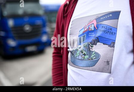 28 agosto 2023, Assia, Gräfenhausen: Roman Koval di Leopoli (Ucraina) indossa una T-shirt per illustrare come i camionisti dell'Europa orientale vengono "schiacciati" da un'azienda di trasporti polacca. Per quasi sei settimane, piloti provenienti dall'Uzbekistan, dalla Georgia e da altri paesi dell'Europa orientale e dell'Asia centrale sono in sciopero nell'area di servizio dell'Assia meridionale. Gli uomini chiedono salari eccezionali. (Al dpa "parlamentare europeo per i conducenti in sciopero: Sono necessari più controlli") foto: Arne Dedert/dpa Foto Stock