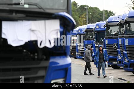 28 agosto 2023, Hesse, Gräfenhausen: Due camionisti passano davanti ai camion allineati. Per quasi sei settimane, i conducenti di un'azienda di trasporti polacca proveniente dall'Uzbekistan, dalla Georgia e da altri paesi dell'Europa orientale e dell'Asia centrale sono in sciopero nella sosta di riposo nell'Assia meridionale. Gli uomini chiedono salari eccezionali. (Al dpa "parlamentare europeo per i conducenti in sciopero: Sono necessari più controlli") foto: Arne Dedert/dpa Foto Stock