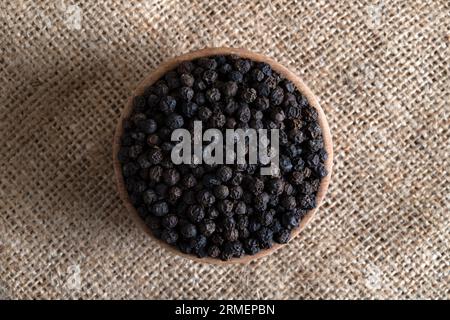 Grani di pepe nero in una ciotola di legno sul sacco da burlap Foto Stock