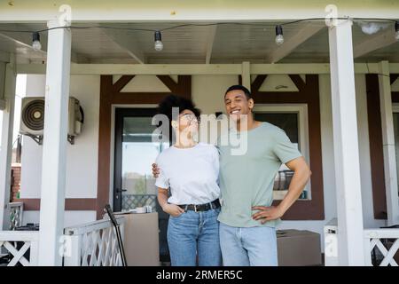 sorridente coppia afroamericana che si abbraccia mentre si trova sul portico di una nuova casa Foto Stock