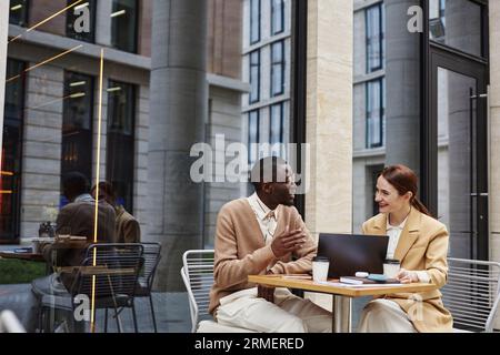 Giovane uomo d'affari fiducioso che spiega qualcosa a una felice collega donna in abbigliamento formalwear durante la discussione sui punti del nuovo progetto Foto Stock