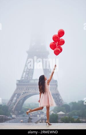 Giovane donna felice in abito tutu rosa con un mazzo di palloncini rossi vicino alla Torre Eiffel a Parigi Foto Stock