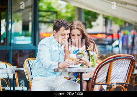 Coppia romantica che beve caffè e cocktail in un caffè all'aperto, leggendo qualcosa sul cellulare. Turisti in vacanza o durante il loro Foto Stock