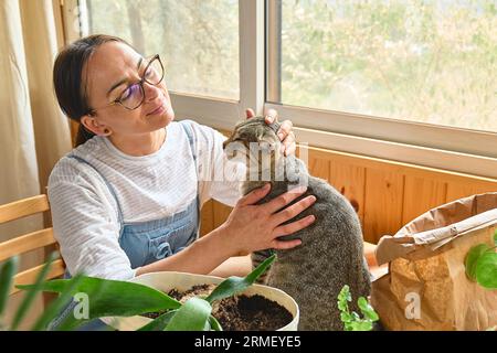 Donna di mezza età che abbraccia e bacia un simpatico gatto tabby in interni. Relazioni uomo-animale. Divertente domestico. Animali domestici senzatetto. Foto Stock
