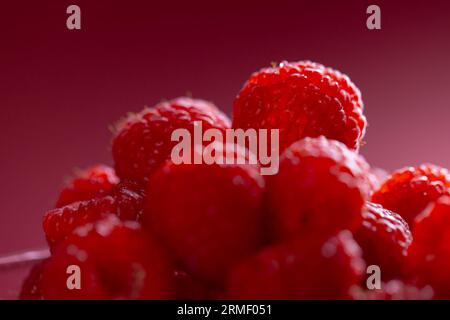 Micro primo piano dei lamponi in un recipiente di vetro con spazio per la copia su sfondo rosso Foto Stock