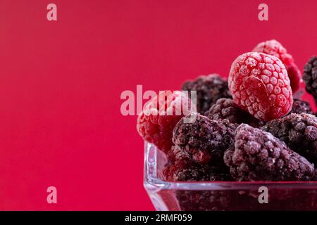 Micro primo piano dei lamponi in un recipiente di vetro con spazio per la copia su sfondo rosso Foto Stock