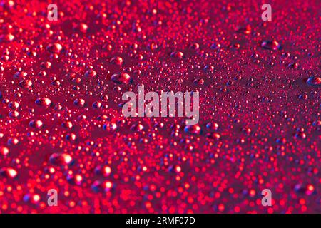 Micro primo piano di gocce d'acqua con spazio di copia su sfondo rosso. Concetto di microfotografia, liquido, texture e colore. Foto Stock